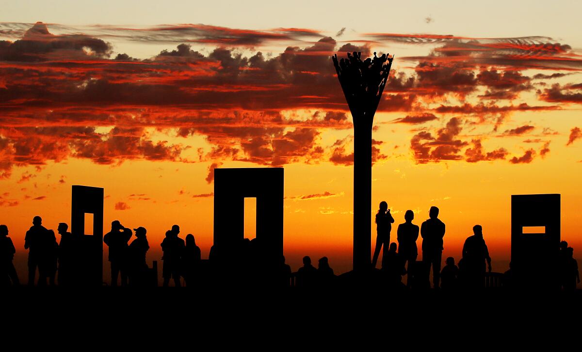 People silhouetted against a red-orange sunset at the top of Signal Hill.