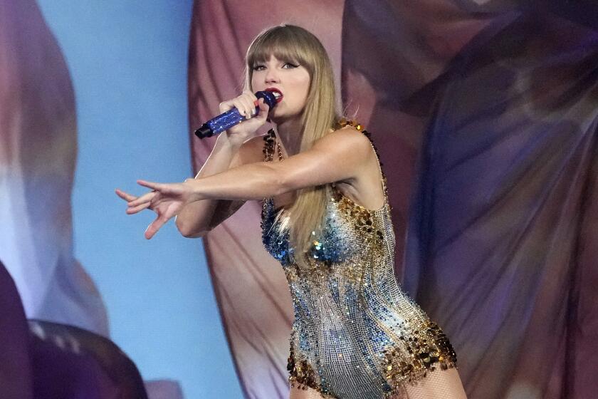 Taylor Swift wears a sparkling romper as she reaches her arm out while singing onstage