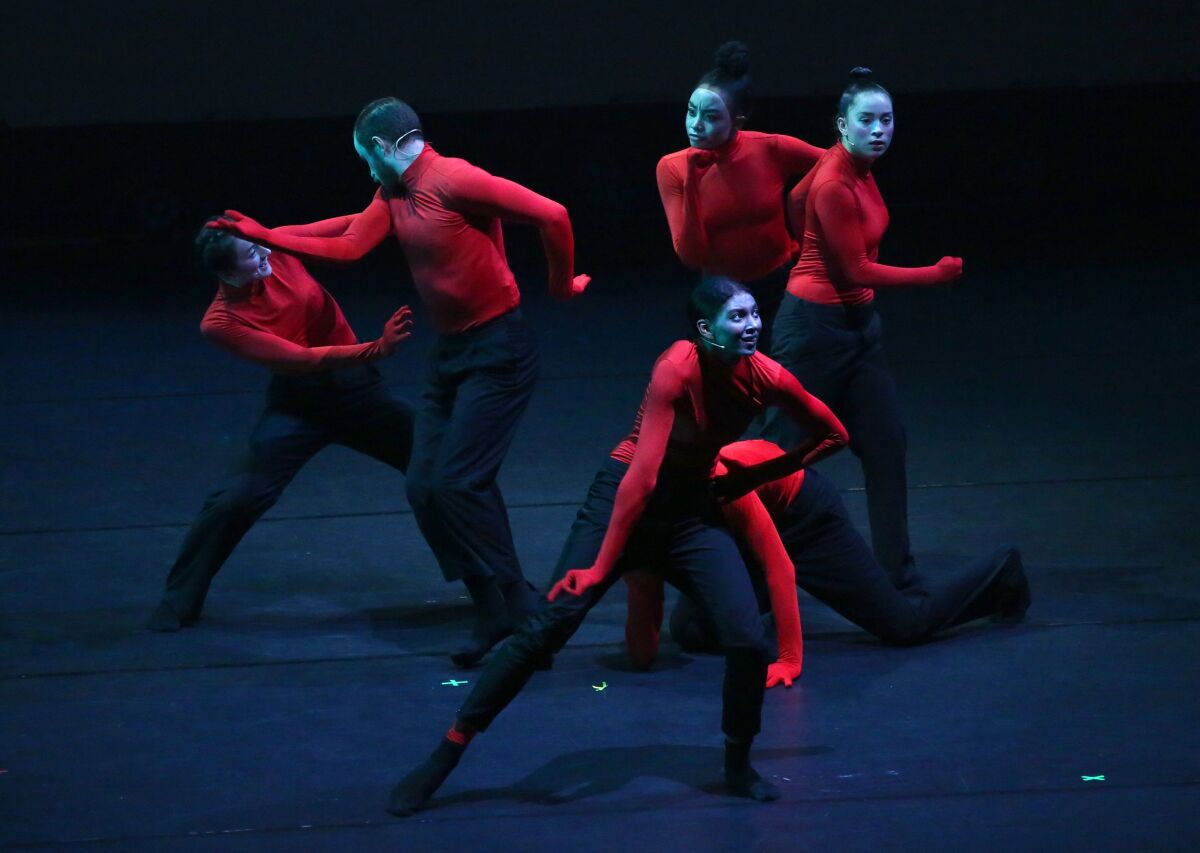 Dancers performing while wearing fitted long-sleeved red tops and black bottoms