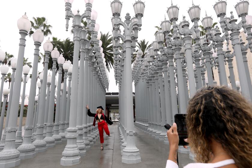 LOS ANGELES, CA - MAY 18, 2020 - - Manon Guijarro, 21, who just graduated from Pierce College, has her personal graduation photo made by friend Paige Johnson, 21, at Chris Burden's outdoor, "Urban Light," at the Los Angeles County Museum of Art in Los Angeles on May 18, 2020. Some outdoor museums can open but LACMA's indoors is still closed but outdoor exhibits are still open to the public. Outdoor museums are among the places that Gov. Gavin Newsom said Tuesday have the green light to reopen in some regions, but that statement has created confusion is places such as Los Angeles County, which is giving museums, outdoor and otherwise, a red light for now. (Genaro Molina / Los Angeles Times)