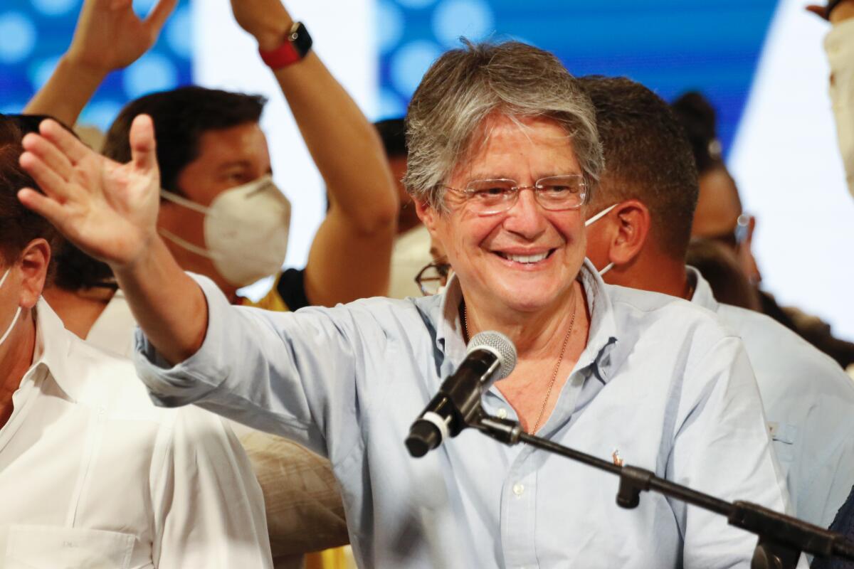 Guillermo Lasso waves and smiles in front of a microphone