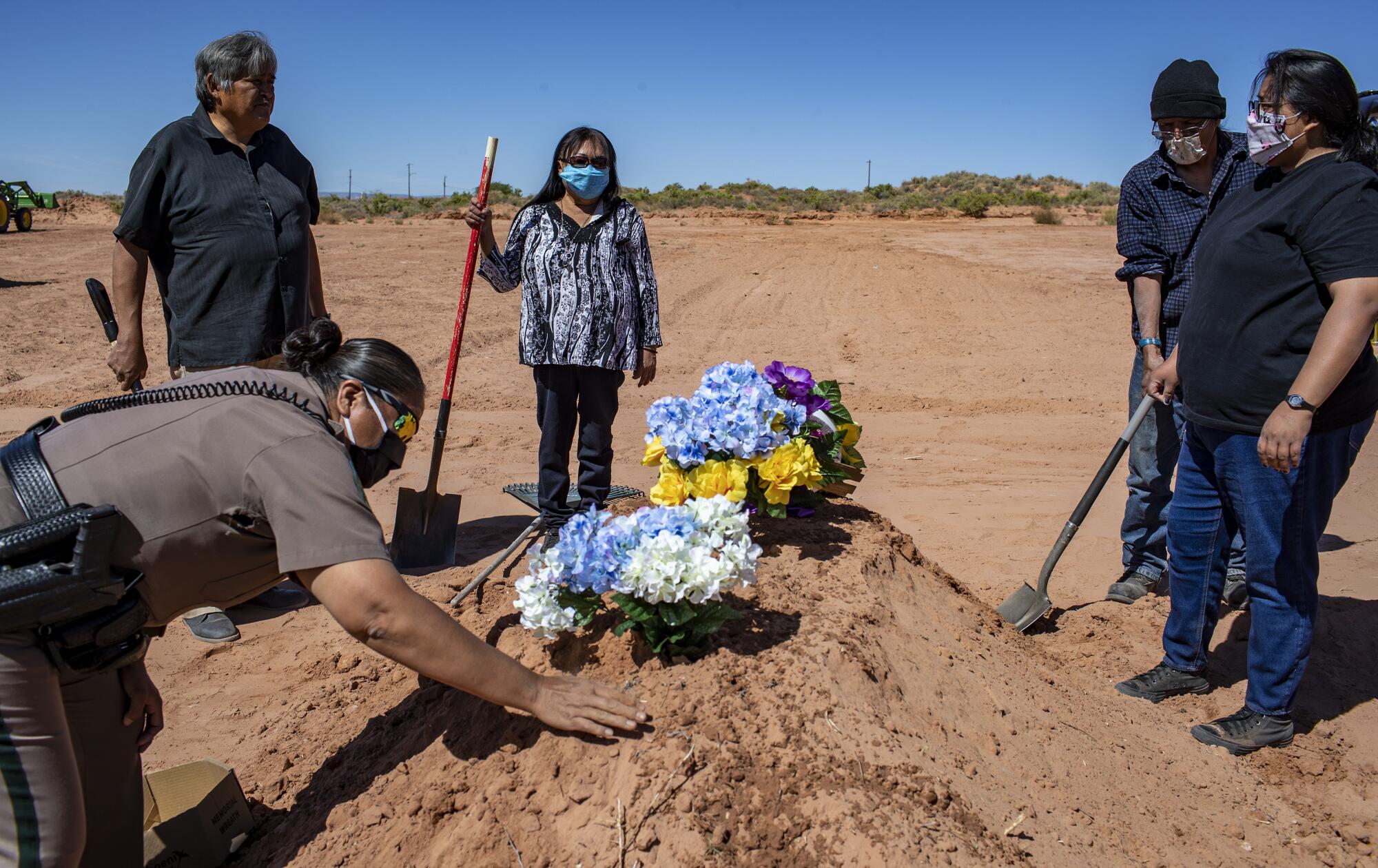 Carlita Bergen, center, holds a shovel as Navajo Nation police officer Carolyn Tallsalt smooths dirt over COVID-19 victim.