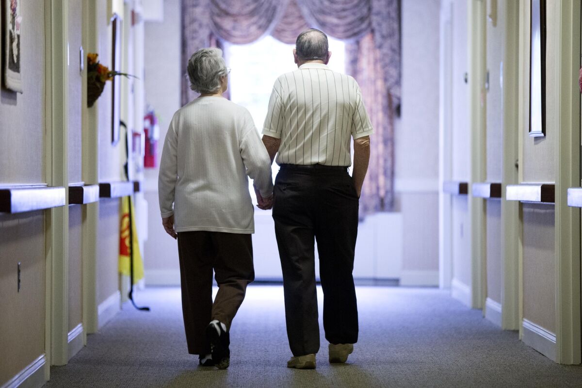 A woman with Alzheimer's disease walks with a companion in a nursing home.