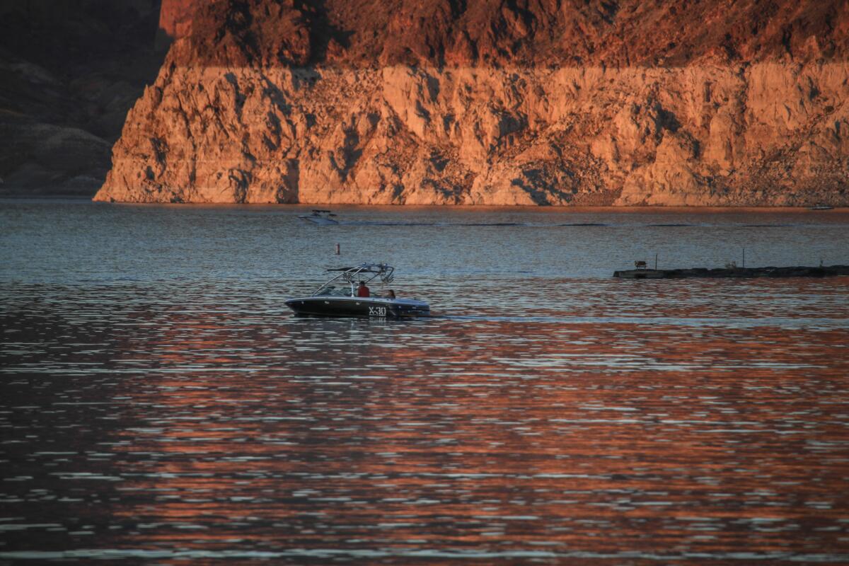 A "bathtub ring" on rock formations at Lake Mead, Nev., with a boat on the water in front of it.