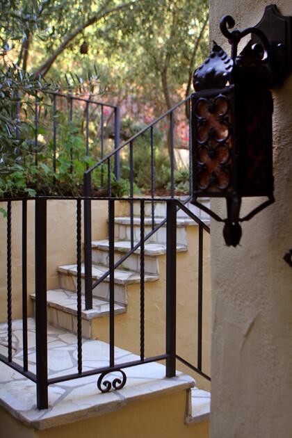 Simple railings and fencing set off the staircase and transition between the lower and upper rear gardens. They were handcrafted by Roberts Iron Works in Azusa, and the lantern was made by Reborn Antiques of Los Angeles. From the double gate at the sidewalk to the Juliet balcony off the master bedroom to the lanterns hanging outside doorways, the metal accents lend vintage ambience.
