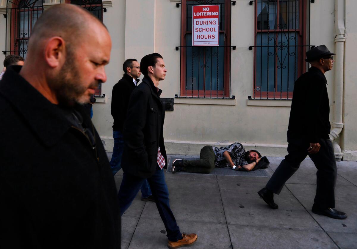 Pedestrians pass a homeless man sleeping on a sidewalk in San Francisco.