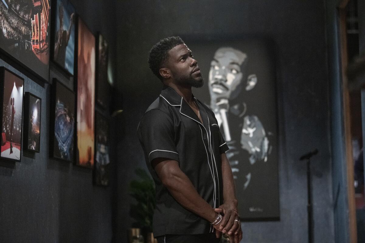 Kevin Hart stands amid portraits of comedy predecessors, including Eddie Murphy.