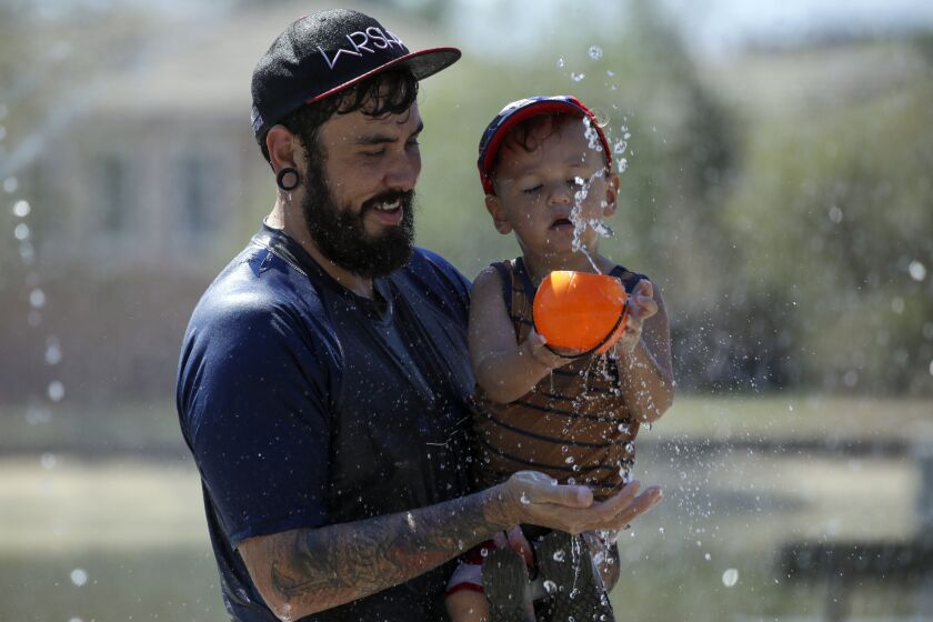 Ontario, CA - September 03: To beat the brutal heat wave that is bearing down on Southern California, with temperatures expected to push into triple-digit temperatures through the Labor Day weekend, Henry Macias, 34, and 2-year-old son Kai Macias, cool off at a splash pad at Cucamonga-Guasti Regional Park on Saturday, Sept. 3, 2022 in Ontario, CA. (Irfan Khan / Los Angeles Times)