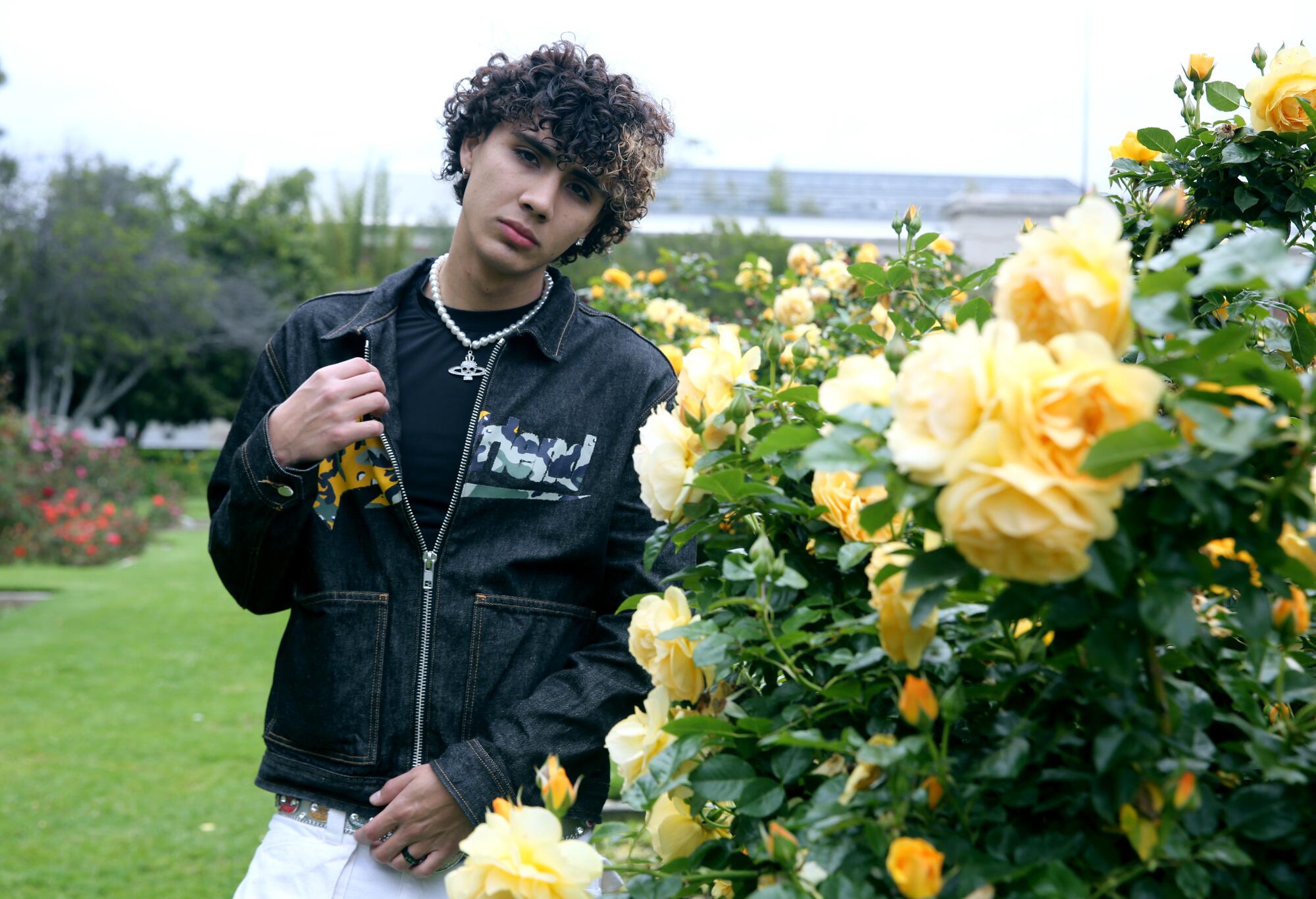 A man in a black jacket and shirt next to a bush of yellow flowers in a park