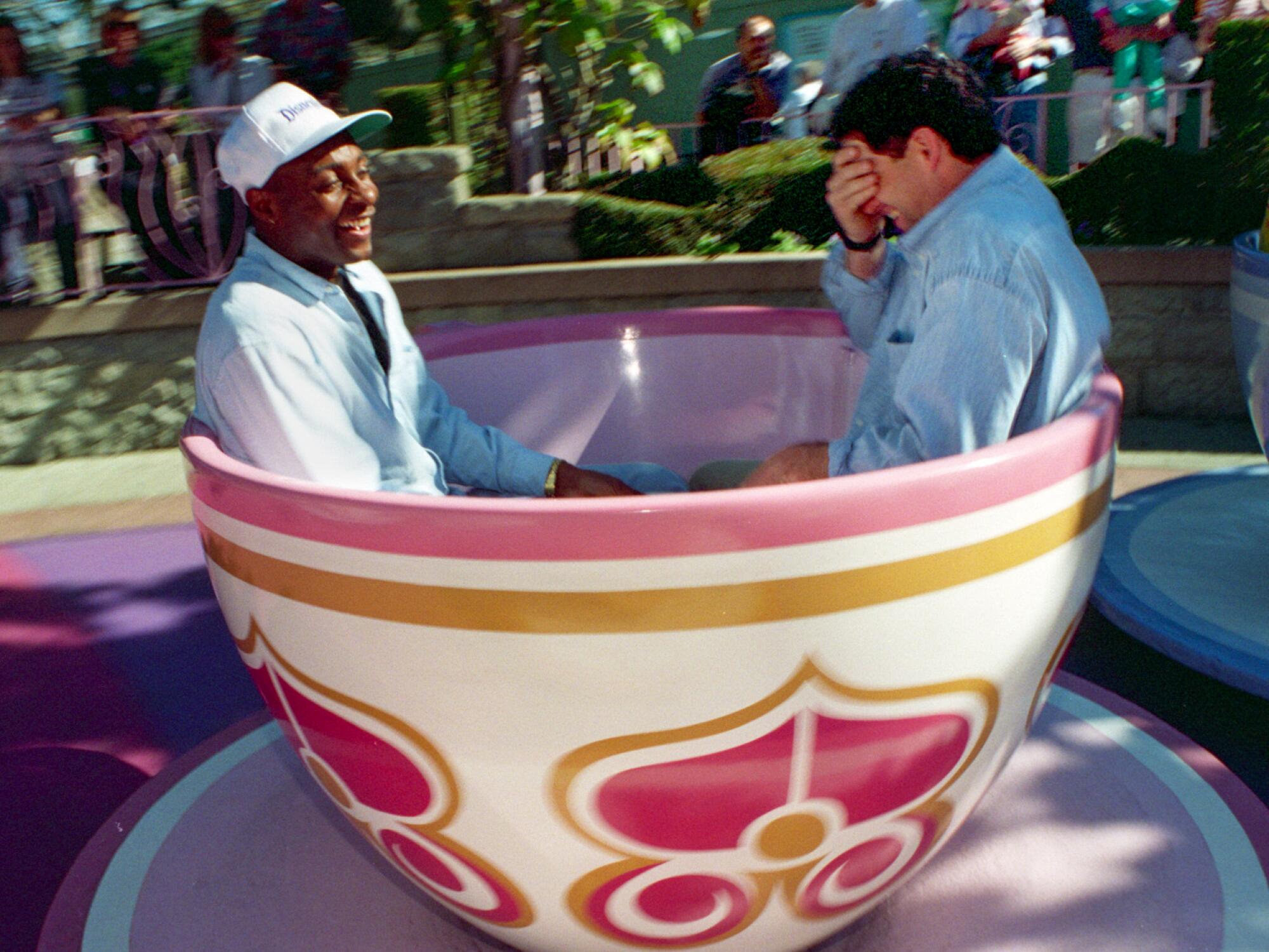 Two men laugh while riding a spinning teacup at Disneyland.