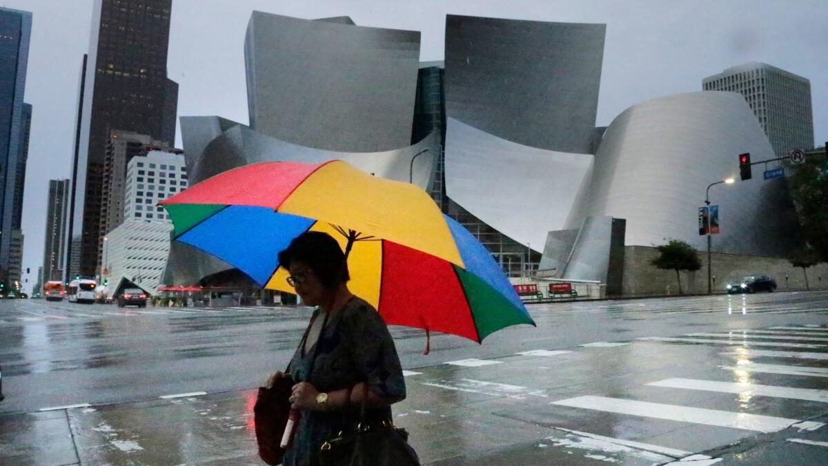 Roads are glistening in morning rain and umbrellas are out in downtown Los Angeles as the first of two storms hits the Southland.