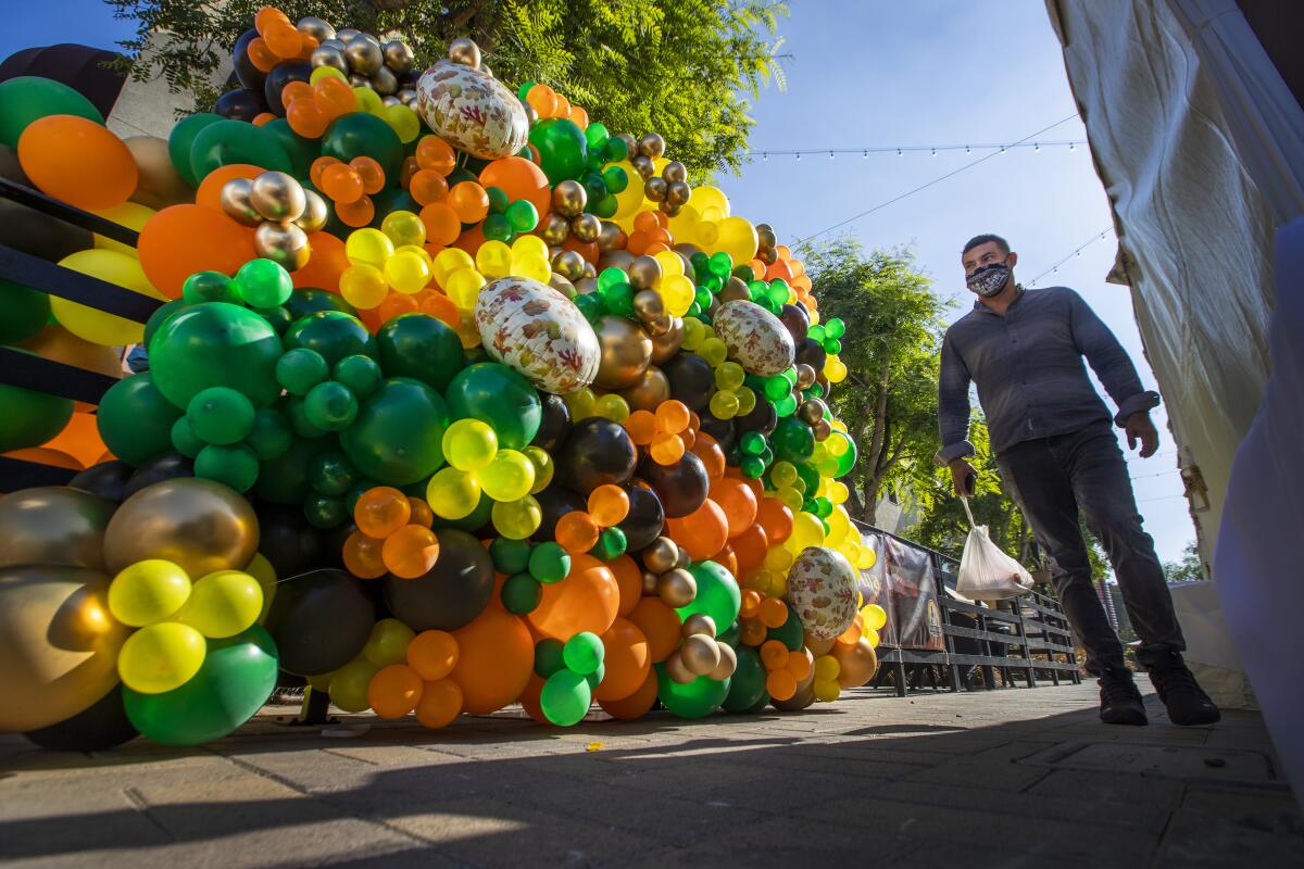 A man in a mask walks past a mound of multicolored balloons.