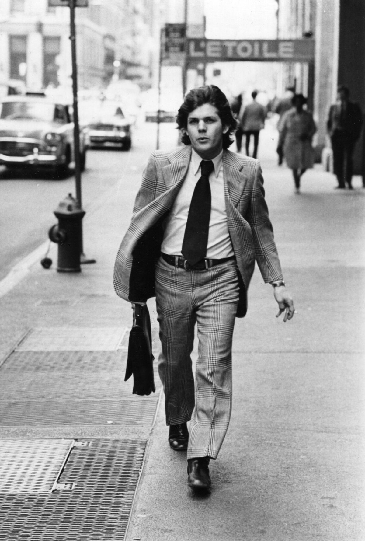 Black and white photo of a man in a suit walking in a city 