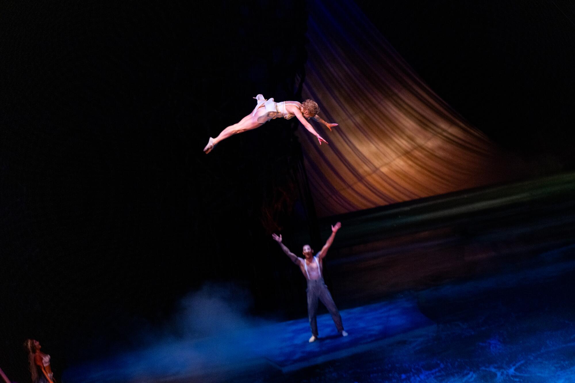 A trapeze artist performs mid-air while another extends his arms onstage during Cirque du Soleil's "O."