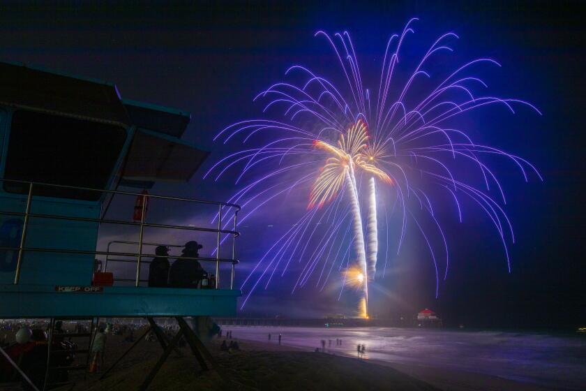 Huntington Beach, CA - July 04: Huntington Beach lifeguards watch the fireworks display over the ocean at the pier on the Fourth of July Sunday, July 4, 2021 in Huntington Beach, CA. A Pier Plaza Festival featured live entertainment & DJs, merchant & crafts vendor booths, amusements & carnival rides, food trucks, beer & wine garden, sponsor activations, live radio broadcasts, and prize giveaways. A Surf City Run 5K kicked off the day and a neighborhood parade that included 3 separate routes replaced the large parade of year's past before the pandemic. The grand finale featured fireworks over the ocean shot off from the pier at 9pm. (Allen J. Schaben / Los Angeles Times)