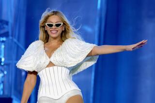 Beyoncé smiles and strikes a pose onstage while wearing a beaded white bodysuit and white cat-eye sunglasses.