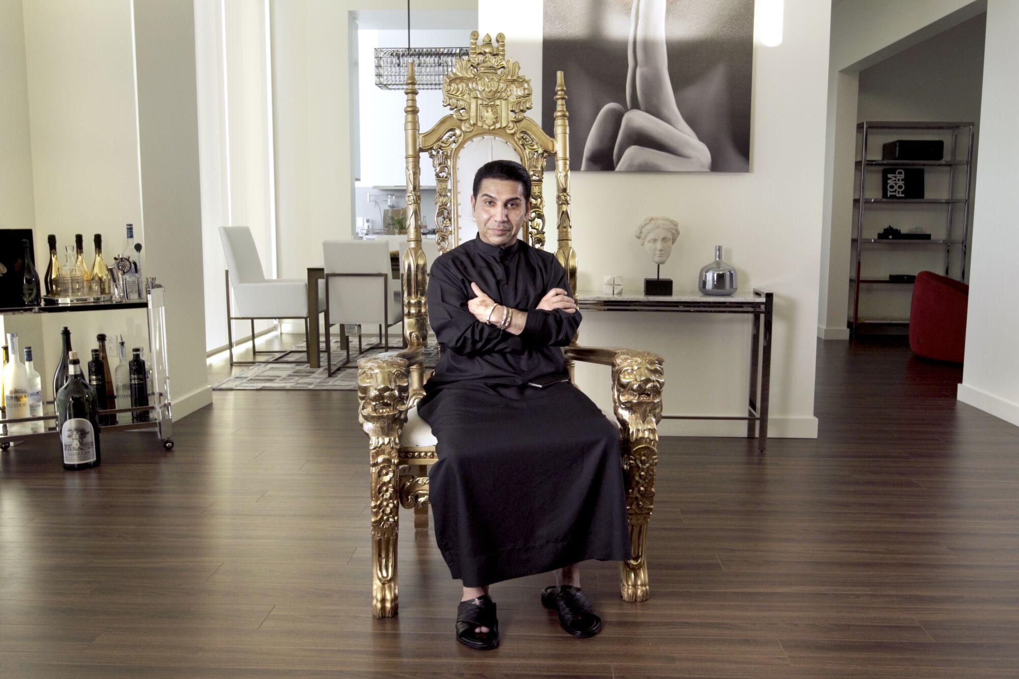 Fereidoun "Prince Fred" Khalilian sits on a gold chair wearing a dark dish dash, arms crossed, looking at the camera smiling
