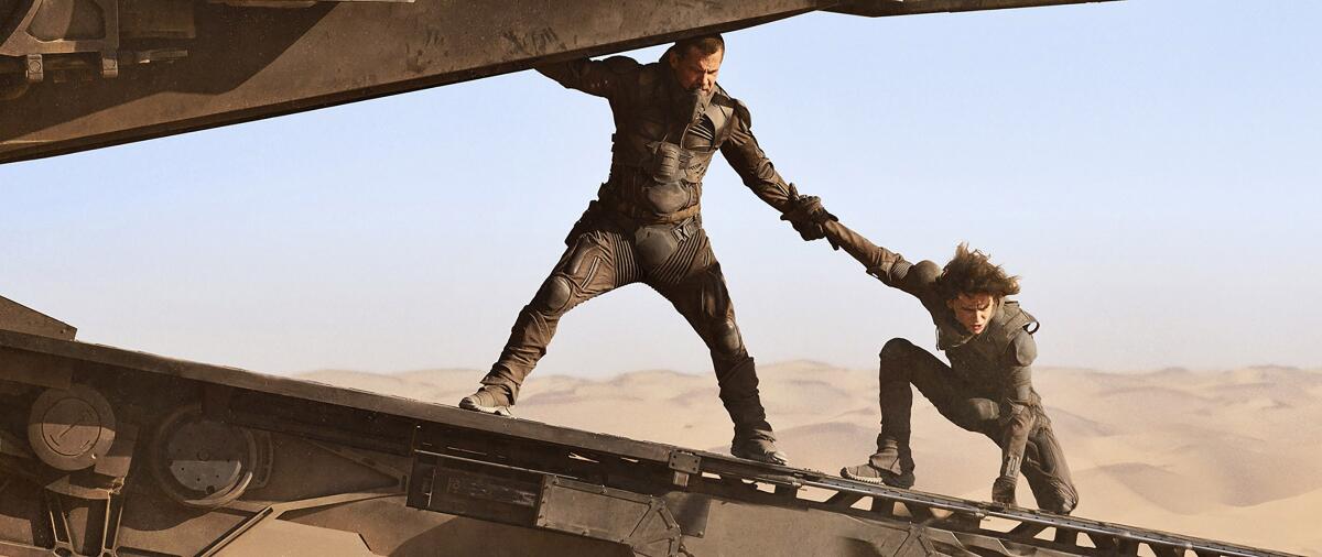 Two men cling to a futuristic craft in the movie "Dune."