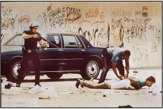 An LAPD officer trains his weapon on men arrested for looting as a State Police officer handciffs one of the suspects on 5/1/1992, on Martin Luther King Blvd. near Vermont Avenue.