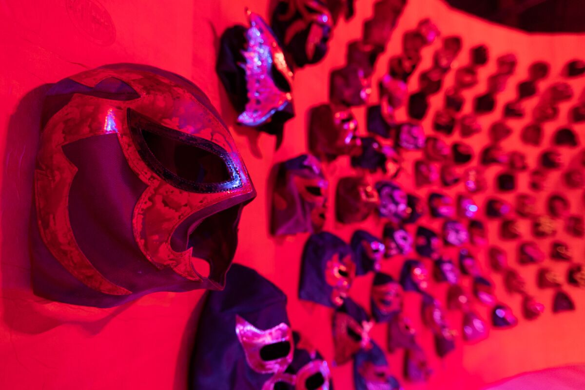 Lucha libre masks are bathed in red light in a production.