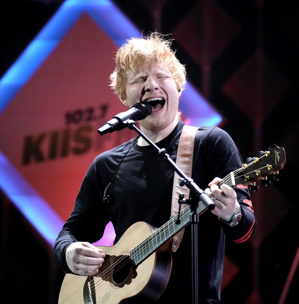 A man dressed in black with an acoustic guitar sings onstage