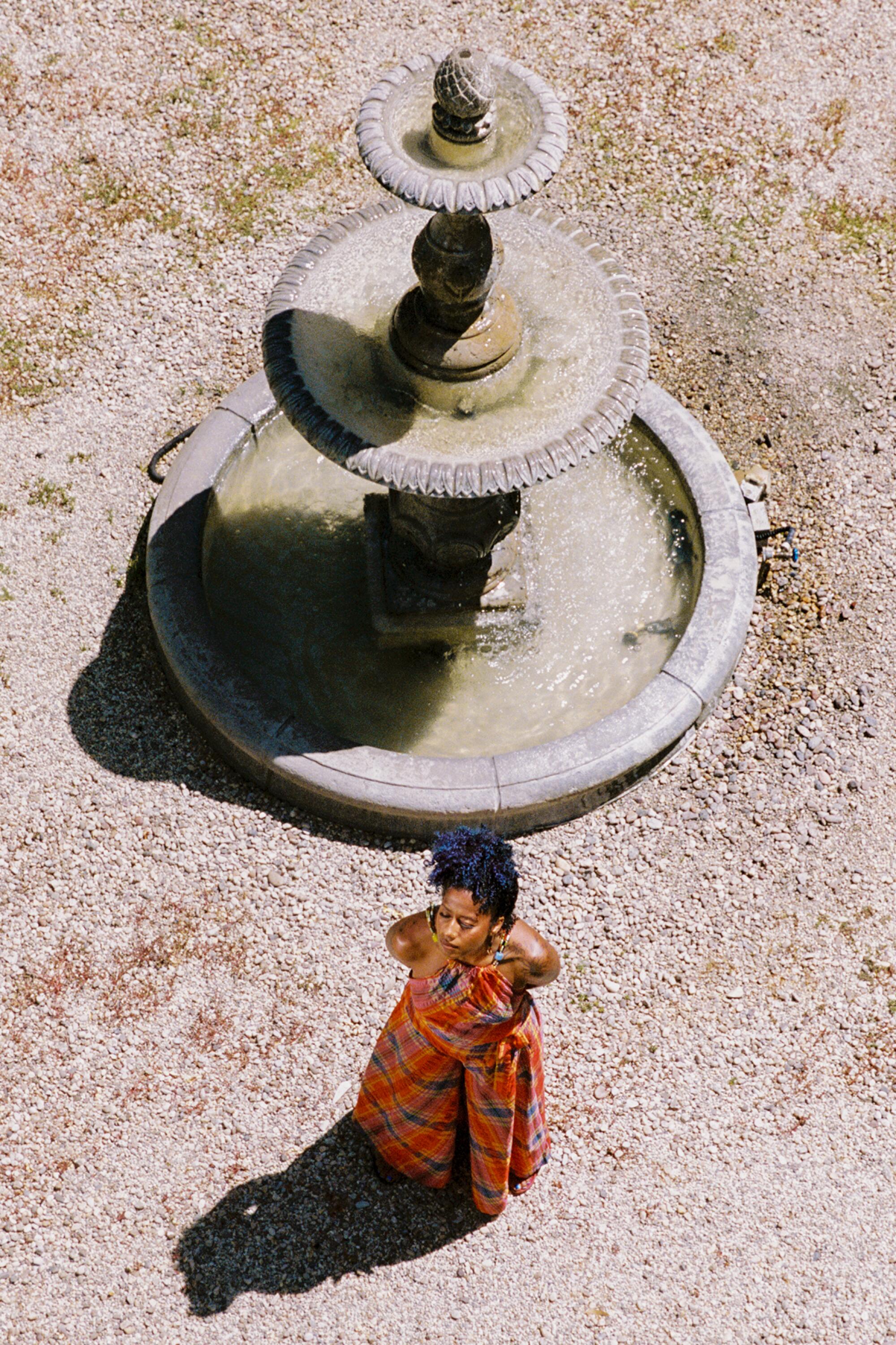 An overhead photo of poet aja monet standing by a large tiered fountain