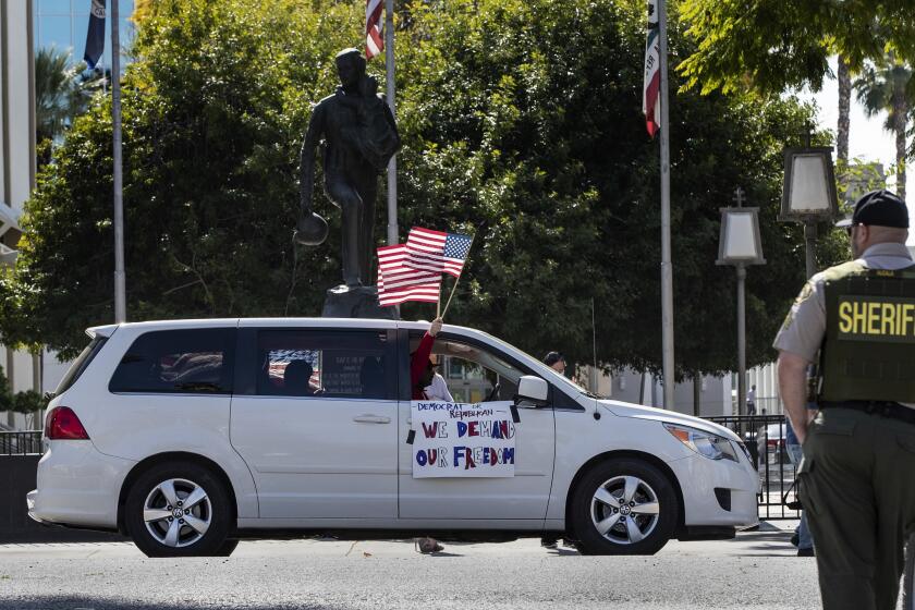 RIVERSIDE, CA- APRIL 21, 2020: A protester waves an American flag at a Riverside County Sheriff Deputy while participating in a car rally to protest conditions in Riverside County jails, where there has been a coronavirus outbreak on April 21, 2020 in Riverside, California. (Gina Ferazzi / Los Angeles Times)