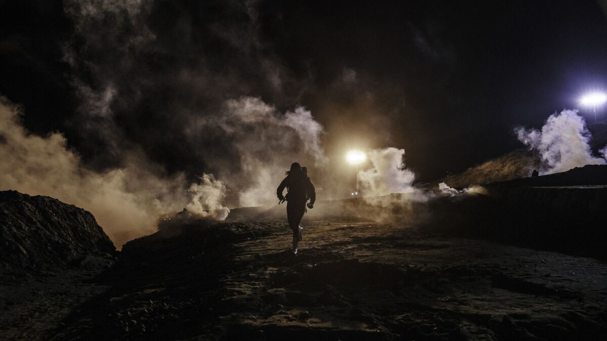 Migrants run as tear gas is thrown by U.S. Border Protection officers to the Mexican side of the border fence after they climbed the fence to get to San Diego, Calif., from Tijuana, Mexico, Tuesday, Jan. 1, 2019.