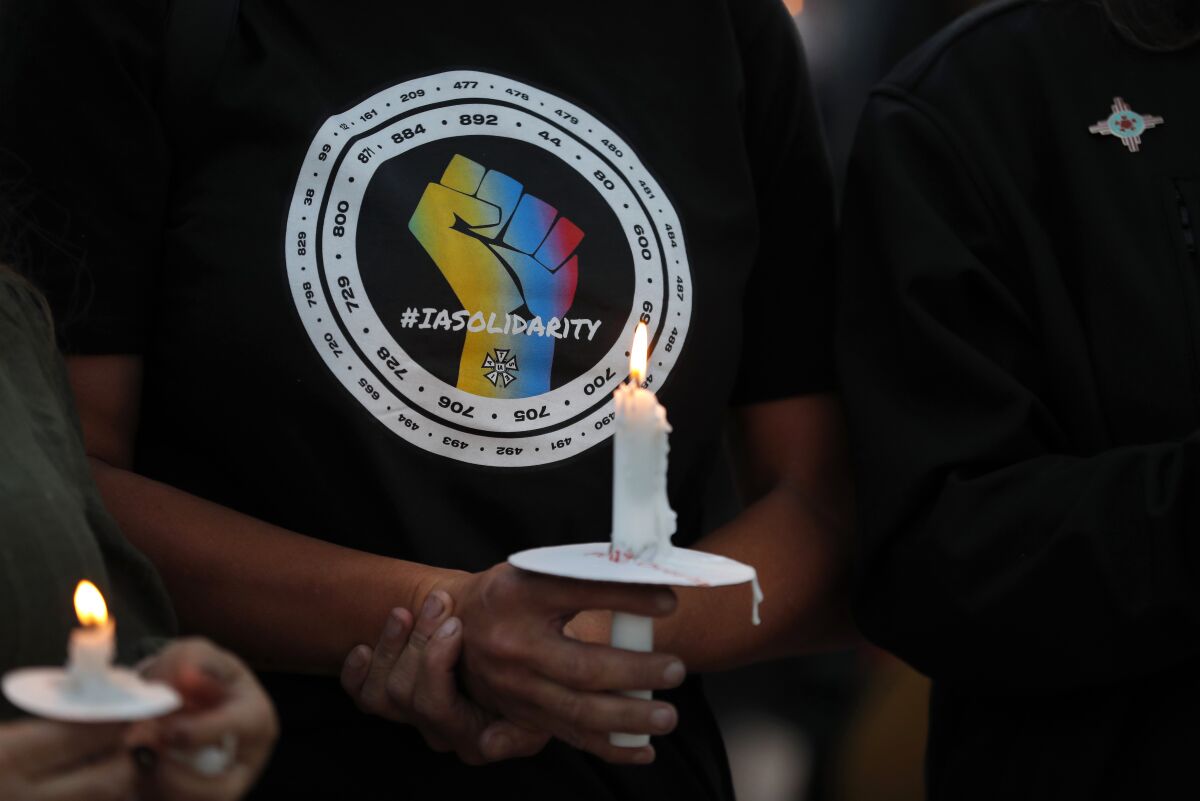 FILE - Movie industry worker Hailey Josselyn, wearing a t-shirt of the International Alliance of Theatrical Stage Employees (IATSA), holds a candle during a vigil to honor cinematographer Halyna Hutchins in Albuquerque, N.M., on Oct. 23, 2021. Hutchins was fatally shot on Thursday, Oct. 21, after an assistant director unwittingly handed actor Alec Baldwin a loaded weapon and told him it was safe to use on the set of a Western filmed in Santa Fe, N.M. Members of the IATSA,will vote on a proposed three-year union contract with Hollywood producers. (AP Photo/Andres Leighton, File)
