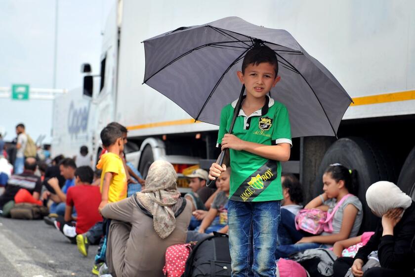 A boy holds an umbrella as migrants and refugees sit on the asphalt of a highway at the official border crossing between Serbia and Hungary, near the northern Serbian town of Horgos, on Sept. 15.