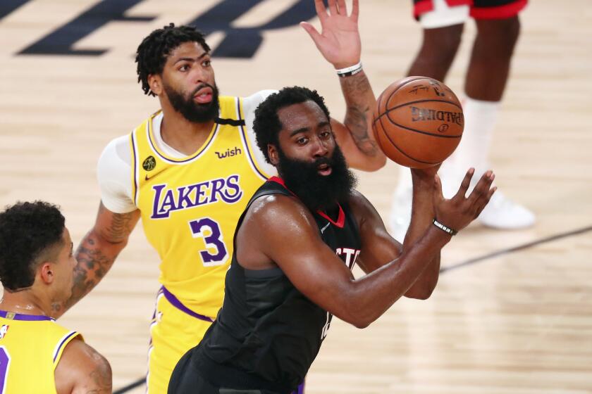 Rockets guard James Harden passes the ball between Lakers forward Kyle Kuzma and forward Anthony Davis.