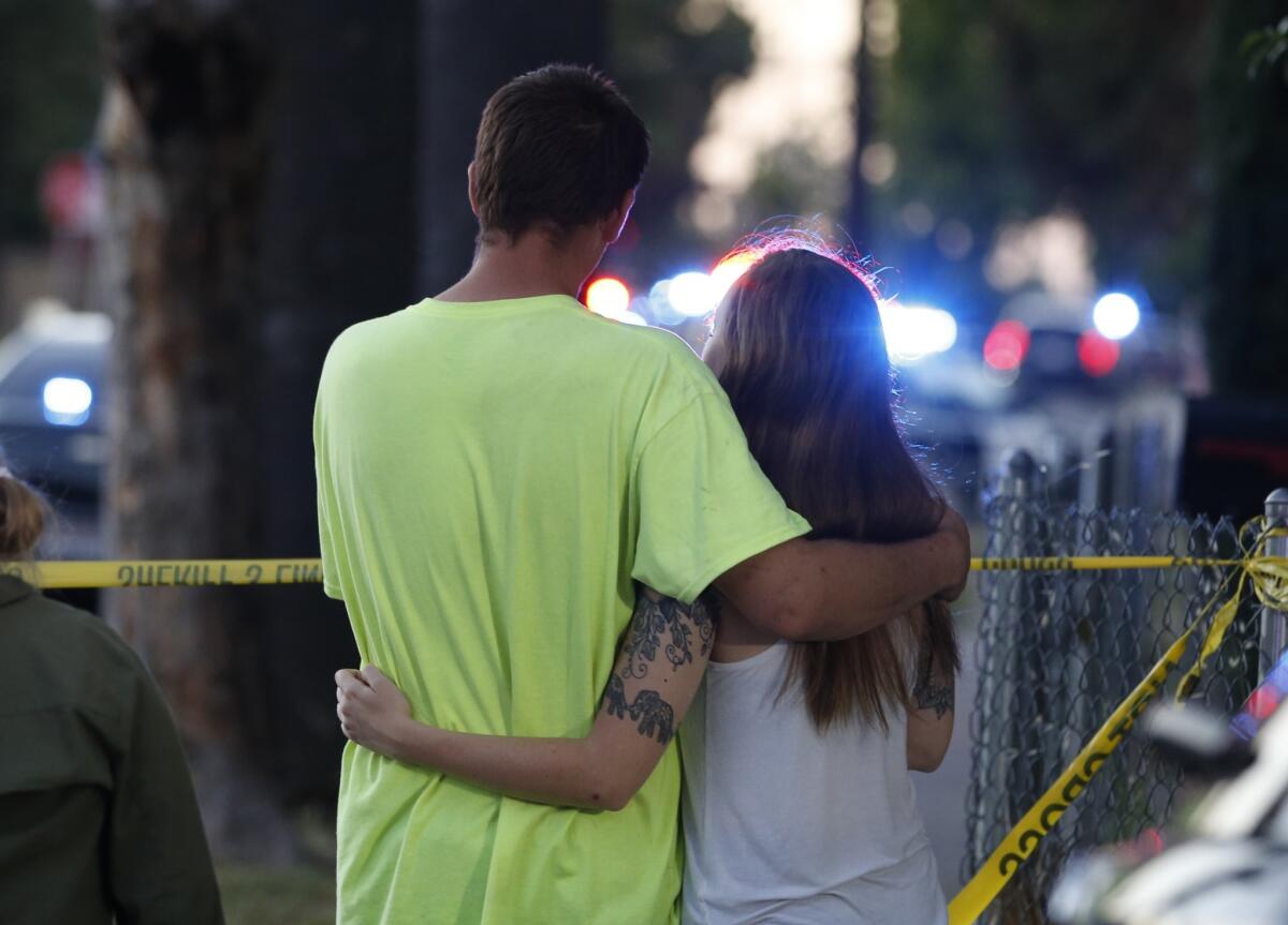 A couple stands near a Sacramento home surrounded by law enforcement. A gunman had holed up there Wednesday night after fatally wounding a city police officer, authorities said.
