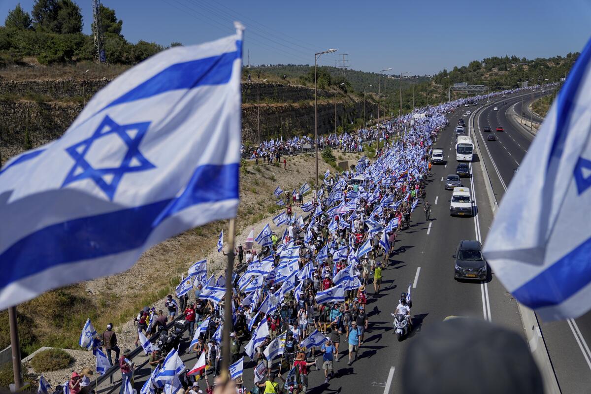 Thousands of Israelis march along a busy highway carrying Israeli flags.