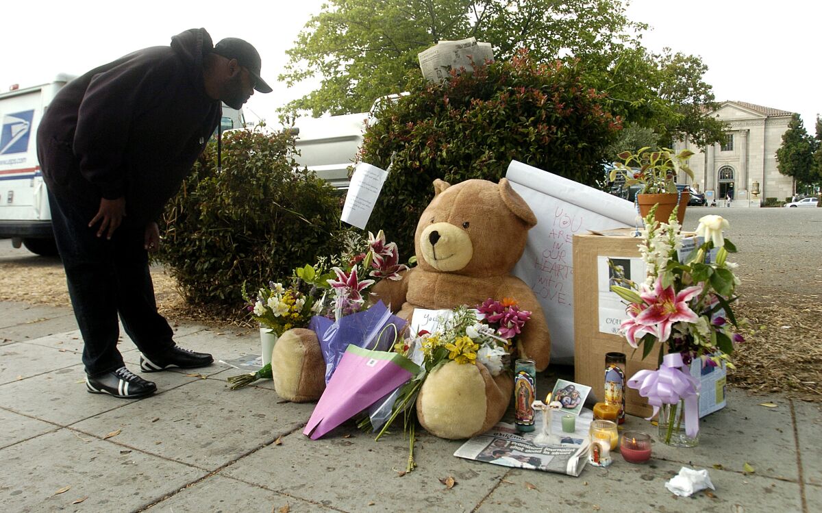   Bir kişi çiçekler, notlar ve bir oyuncak ayıdan oluşan bir sokak anıtına bakar.