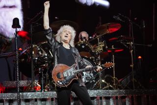 Brian May of Queen raises his right hand while playing guitar onstage