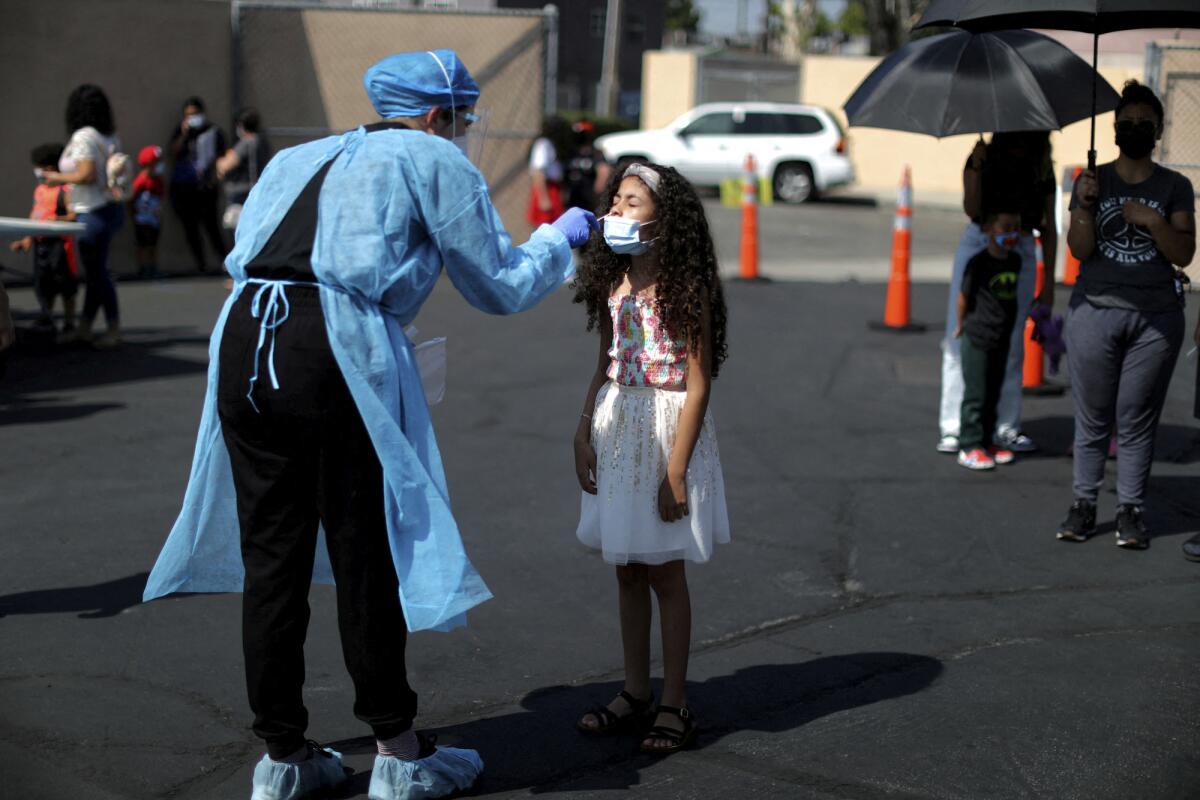 A young girl has her nose swabbed by a woman in protective gear in a parking lot