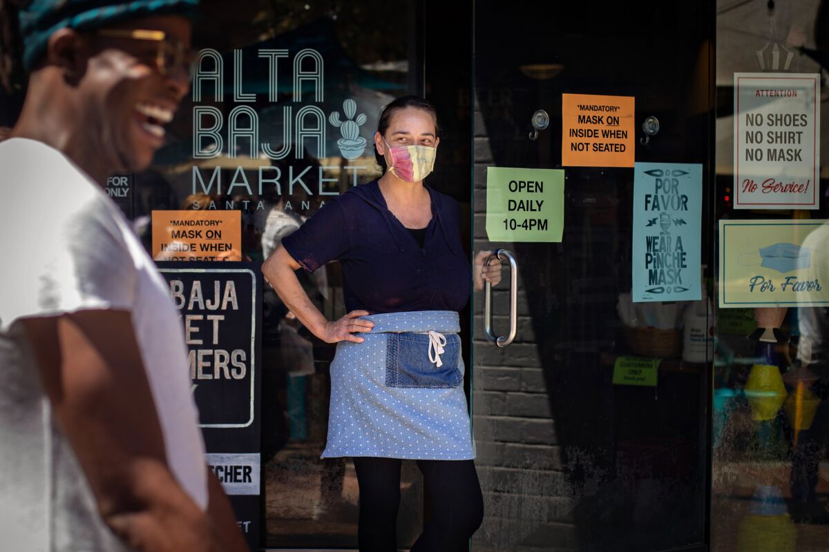 A woman wearing a mask stands at the door to a market.
