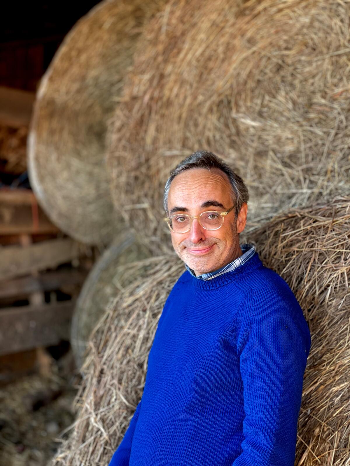 Gary Shteyngart standing against hay with blue sweater and glasses