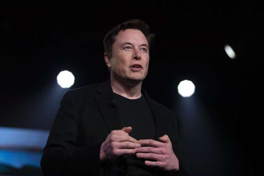 Tesla Chief Executive Elon Musk speaks in a dark room with spotlights. 