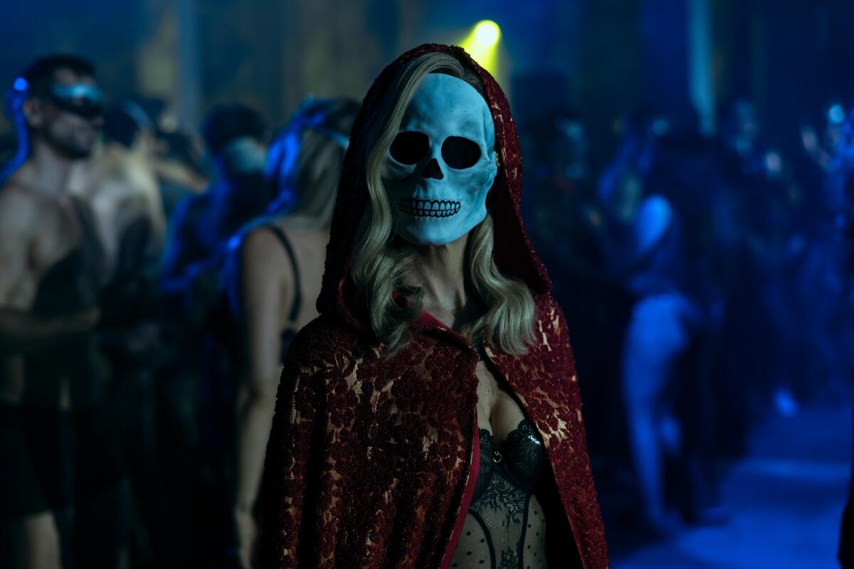 A woman in a red lace cape and skull mask.