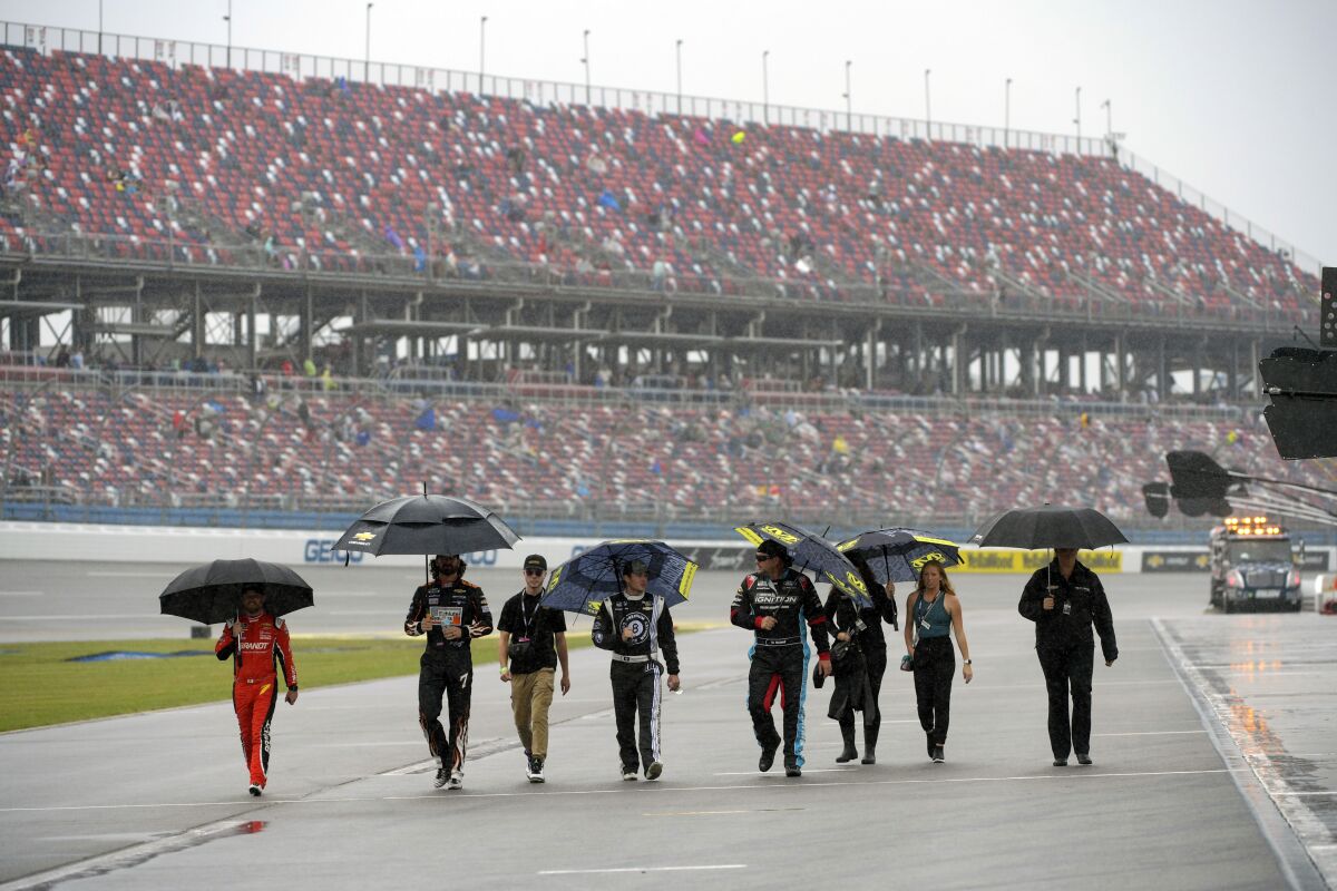 Team members walk through pit row in the rain before a NASCAR Cup series auto race Sunday, Oct. 3, 2021, in Talladega, Ala. (AP Photo/John Amis)