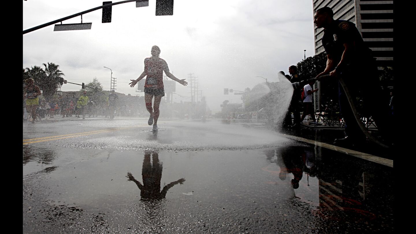 A race participant runs through water sprayed by firefighters at the 19th mile during 30th Los Angeles Marathon.