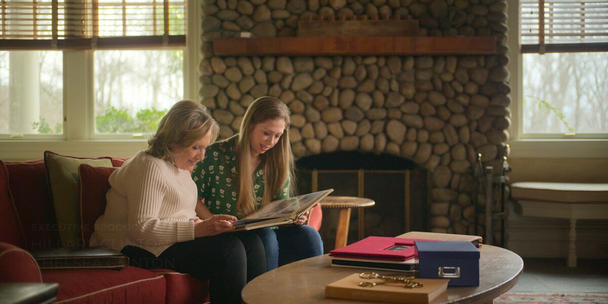 Hillary Clinton, left, and Chelsea Clinton look over a scrapbook in a living room with a stone fireplace