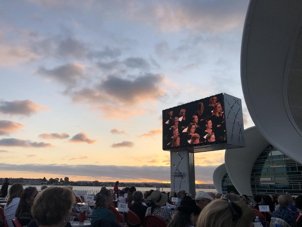A giant video monitor shows the San Diego Master Chorale. Behind it is the setting sun on the bay. 