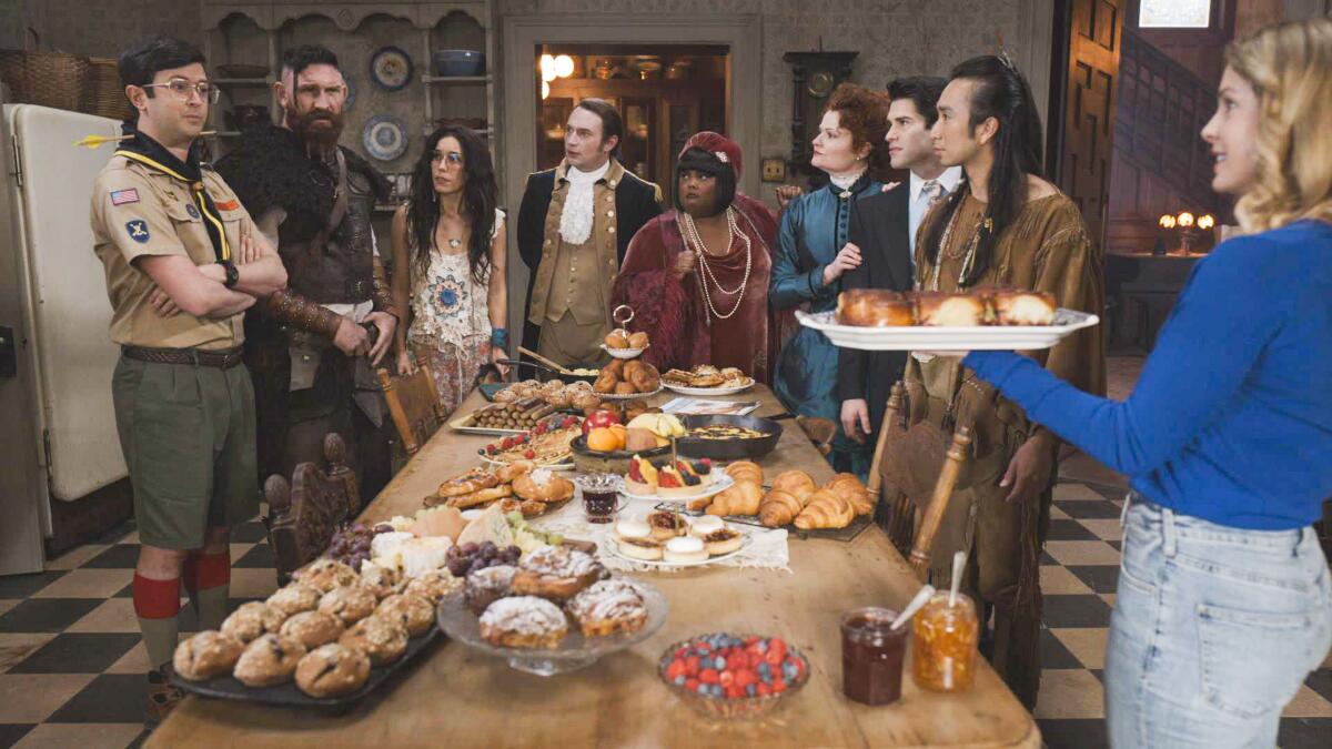 People from different historical eras encircle a table piled with baked goods