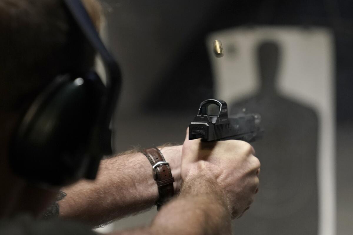 A view of a man holding a pistol with both hands, aimed at a silhouette of a person in a shooting range 