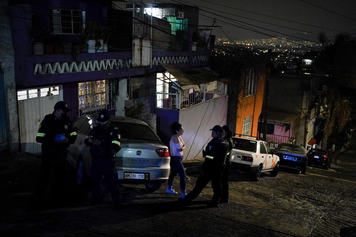 Police talk to a woman outside, on a hilly street next to parallel-parked cars