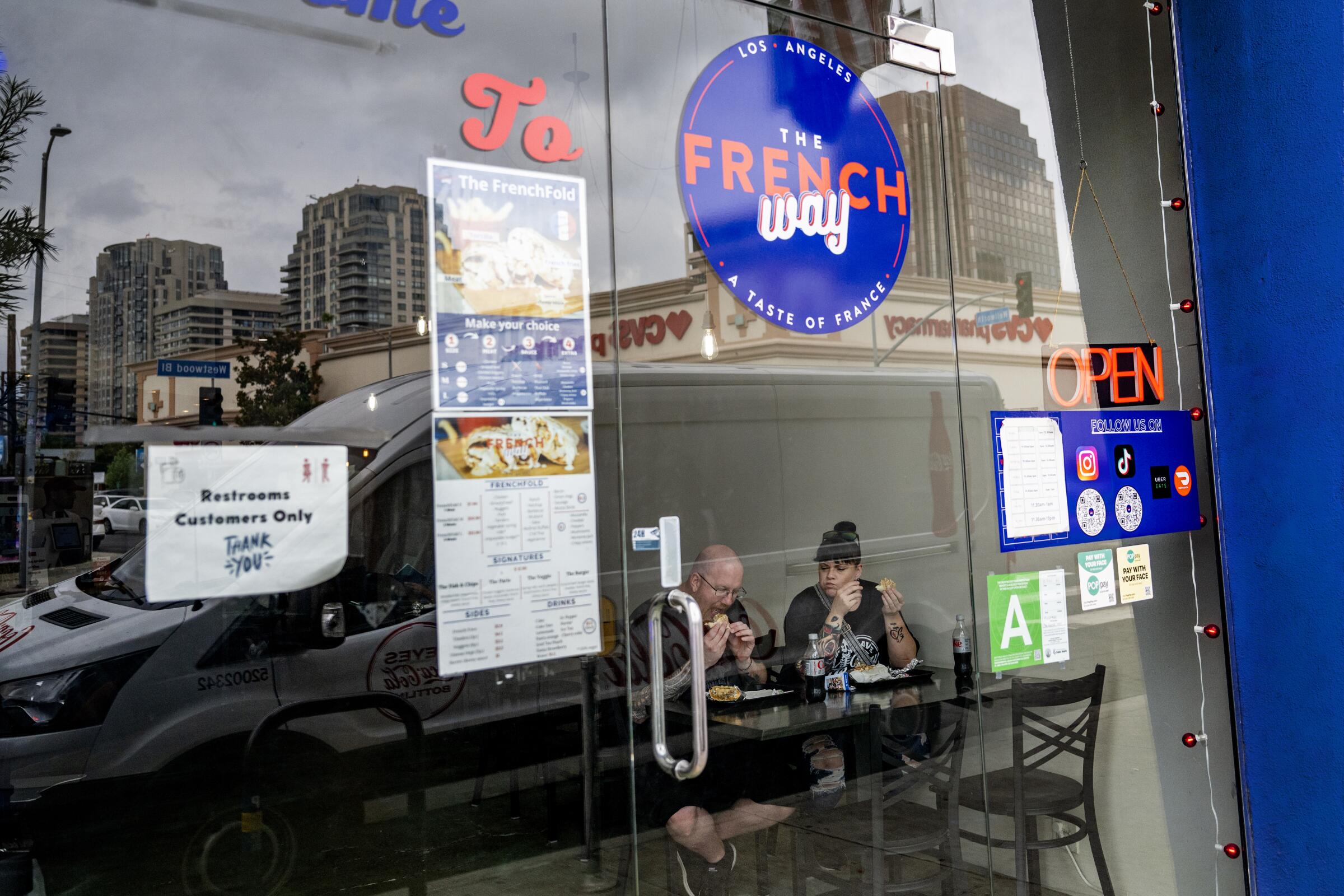 People eat while seated behind a glass door that says "The French Way"