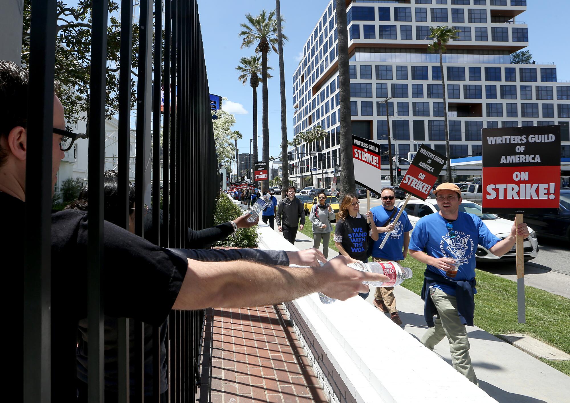 People inside the Sunset Bronson Studios hand bottles of water to striking Writers Guild of America workers on May 2.