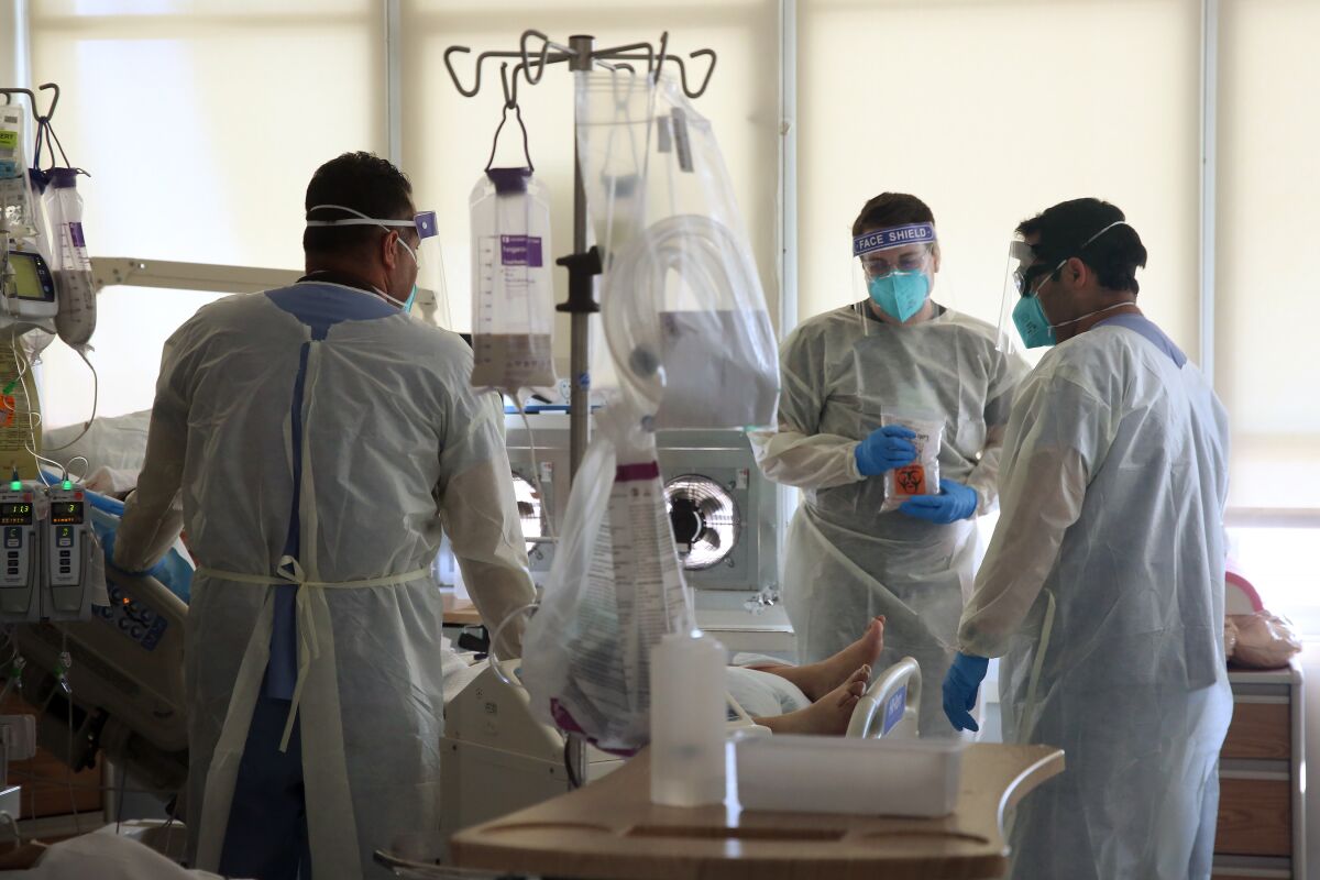 Healthcare workers in protective gear surround a hospital bed